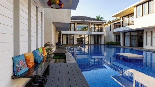 A modern hotel with a large indoor swimming pool, a wooden deck, and colorful cushions. - Casa Amore Aqua Sol (Vagator)