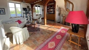 A cozy living room with a wooden ceiling, a white sofa, a red rug, and a bookshelf. - Domaine de Bel Ebat offers a peaceful, green setting (1h from Paris) (Paucourt)