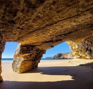 Uma praia com uma formação rochosa natural em arco sobre a areia.