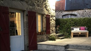 Ein Steinhaus mit roter Tür und verhängten Fenstern, einer hölzernen Bank und einem Blumentopf.