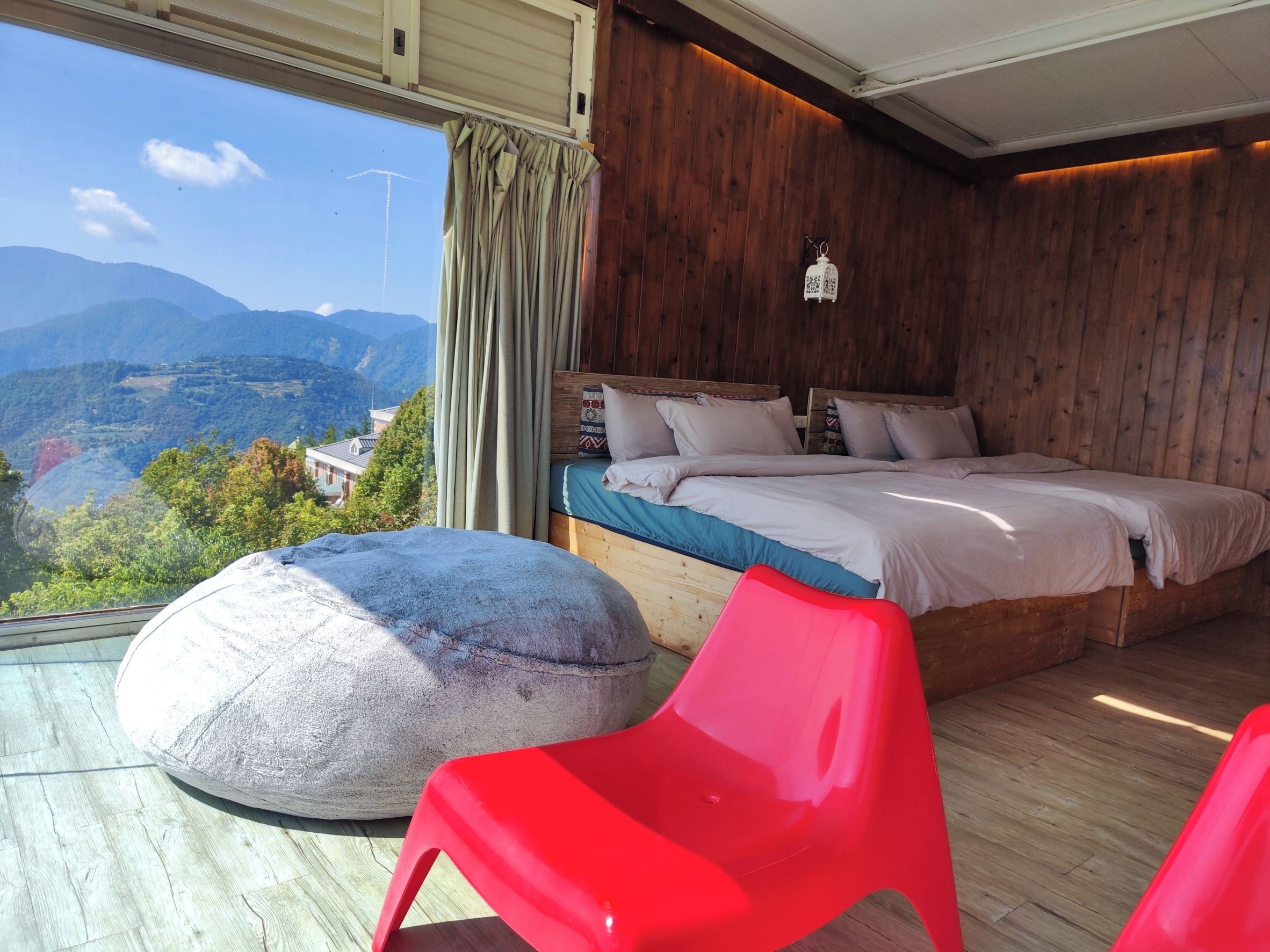 A bedroom with a large bed, wooden walls, a view of mountains, and a red chair.