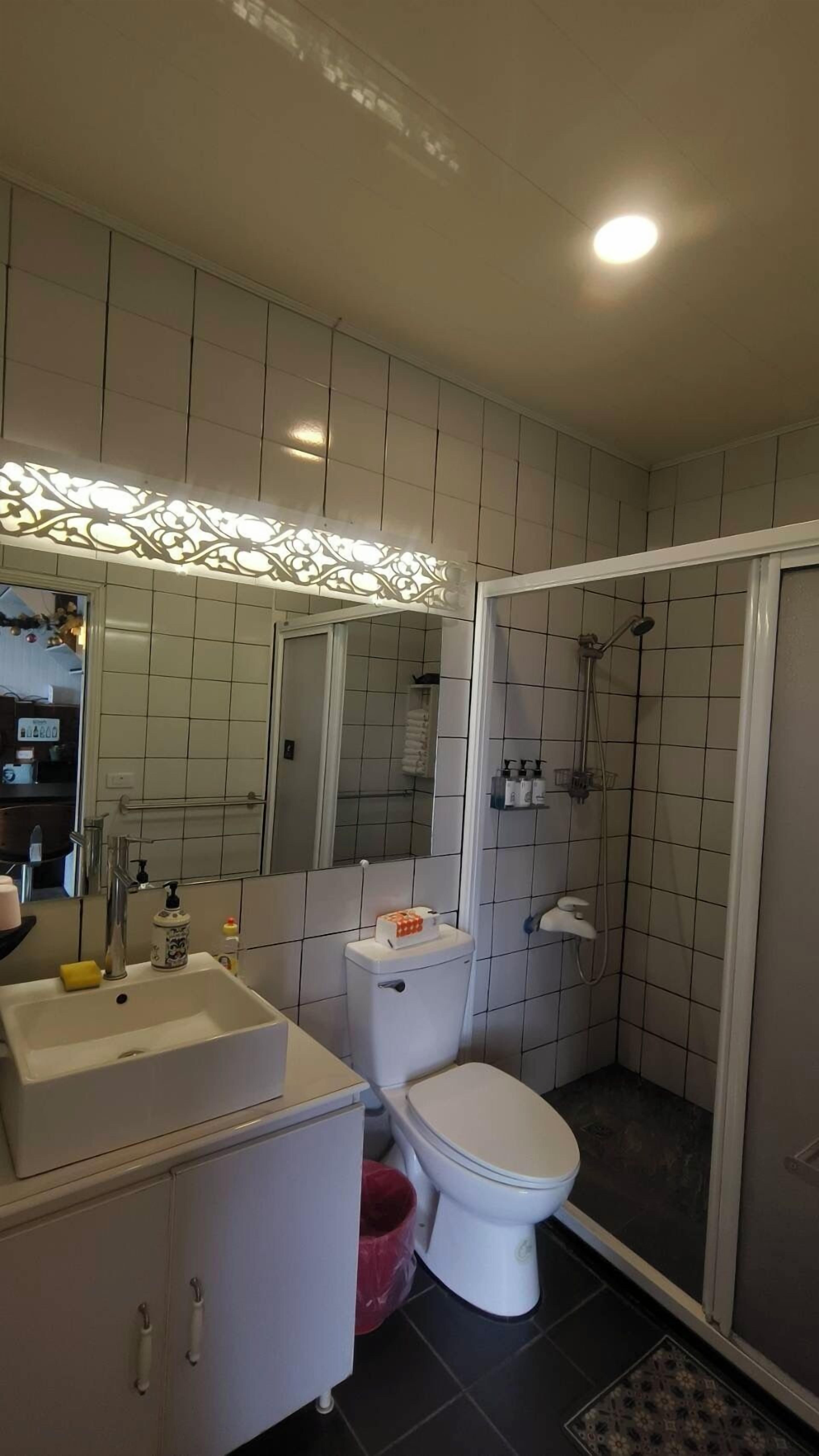 A bathroom with a white sink, toilet, and shower. There is a mirror above the sink and a tiled shower area.