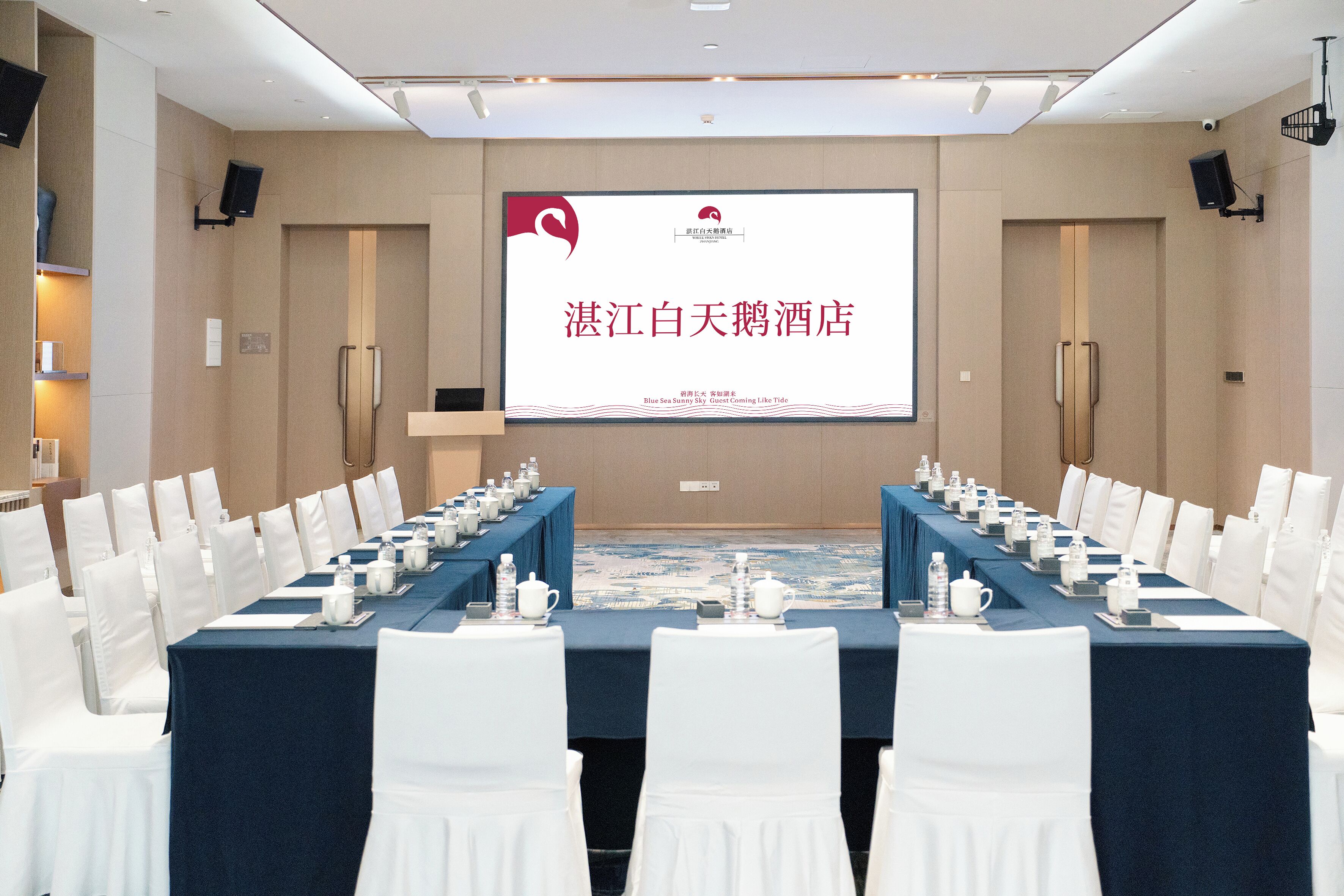 A conference room with a long table, white chairs, and a presentation screen.