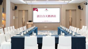 A conference room with a long table, white chairs, and a presentation screen.