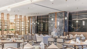 A modern restaurant with multiple dining tables and chairs, marble walls, and pendant lighting.