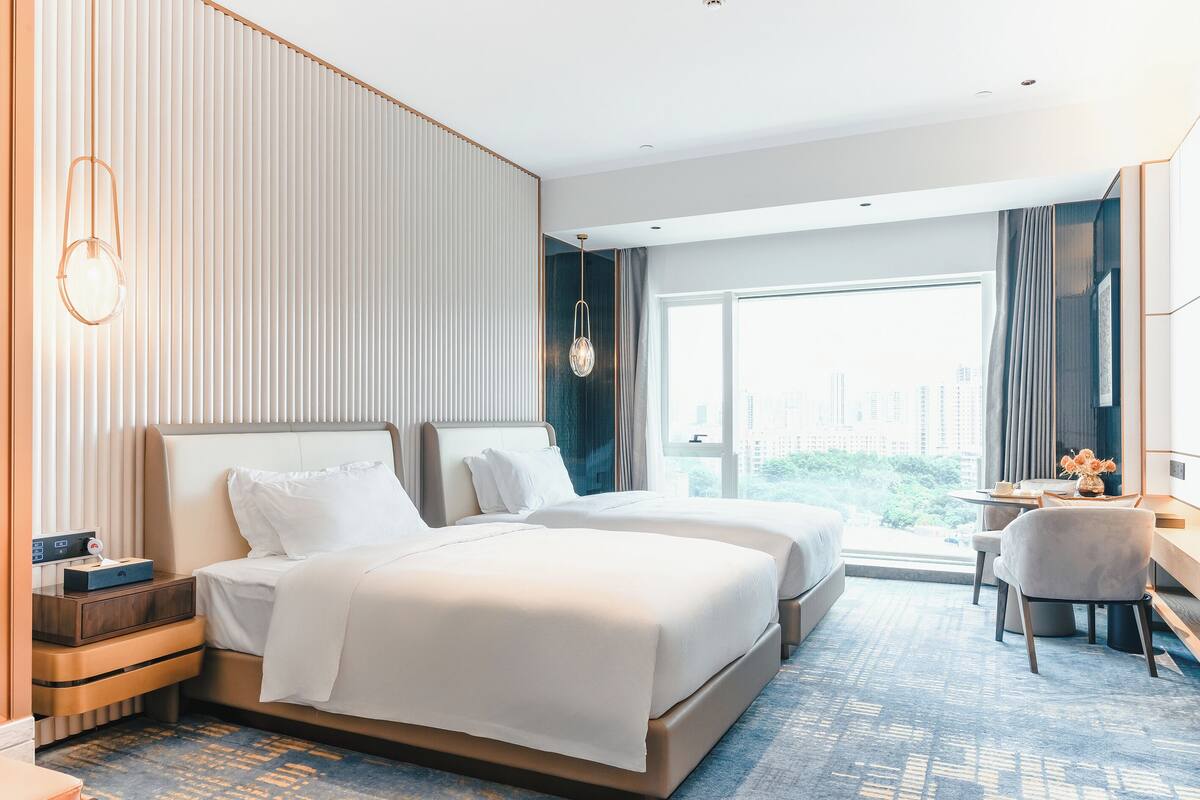 A hotel room with two beds, a desk, and a view of the city.