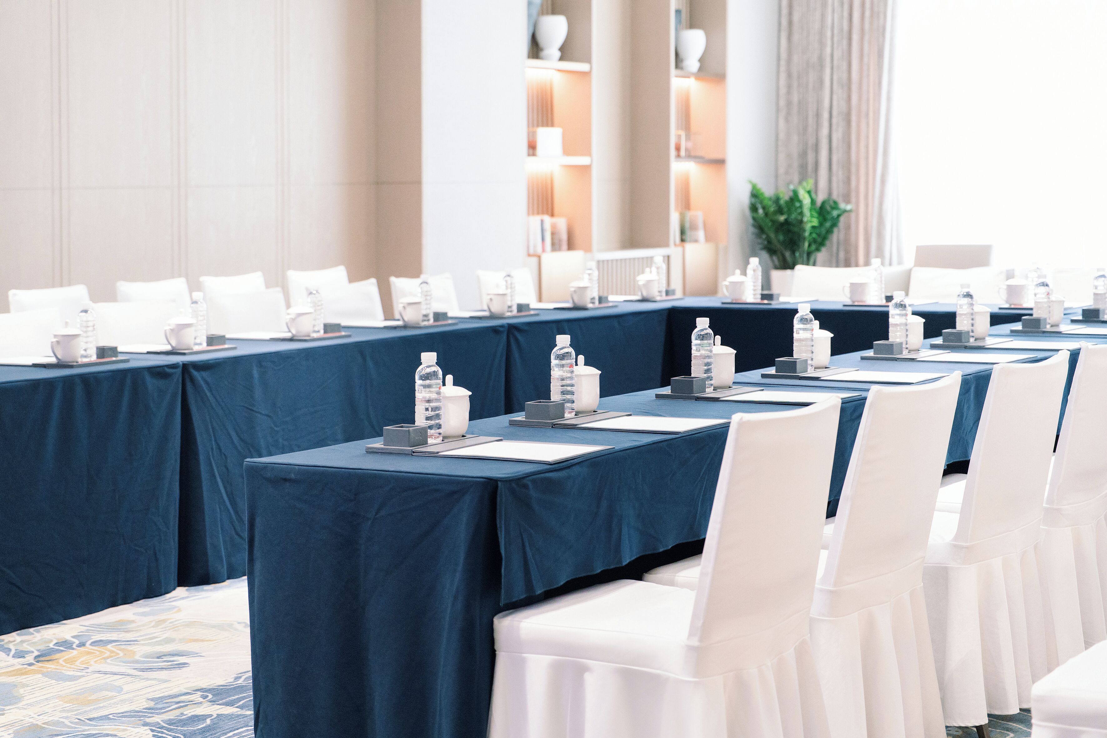 A conference room with multiple tables, each set with water bottles, notepads, and pens.
