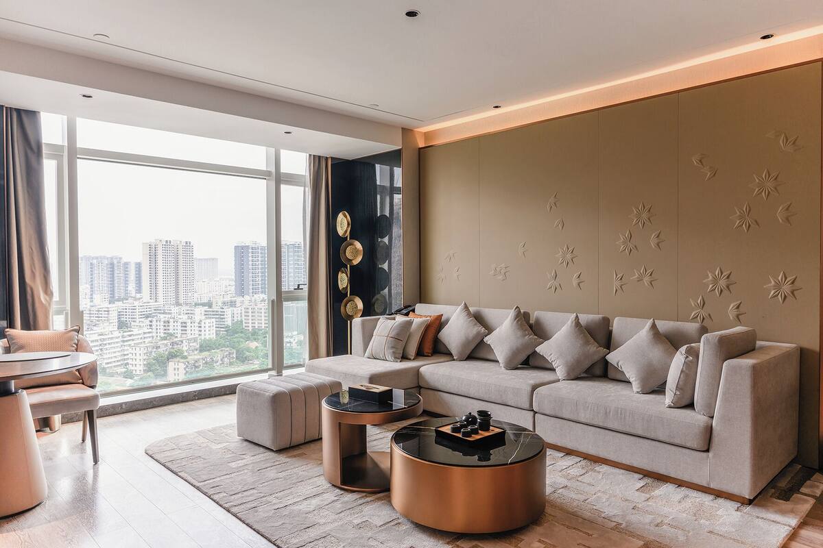 A modern living room with a sofa, two coffee tables, and a view of a cityscape through large windows.