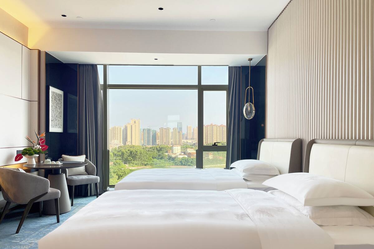 A hotel room with two beds, a desk, and a view of the cityscape.
