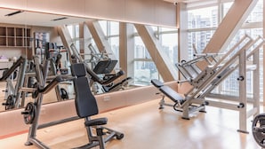 A modern gym with various exercise equipment, large windows, and a city view.