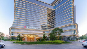 A modern hotel with a curved facade, large glass windows, and a well-maintained entrance area with a landscaped garden.
