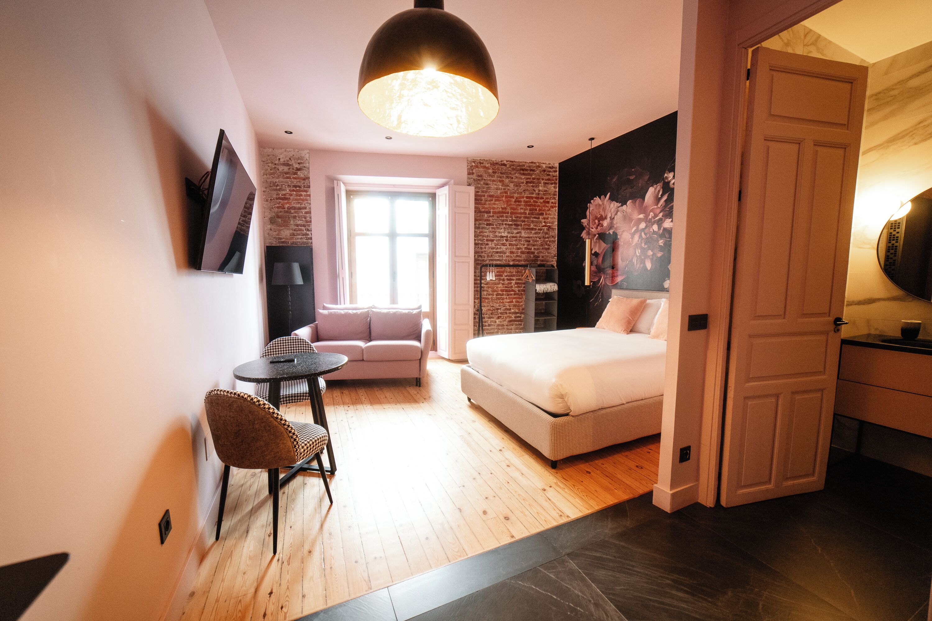 A modern bedroom with a bed, a sofa, a small table, and a TV mounted on the wall.
