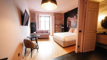 A modern bedroom with a bed, a sofa, a small table, and a TV mounted on the wall.