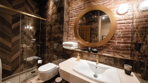 A modern bathroom with a glass shower enclosure, a white toilet, and a large sink with a gold faucet. - Rincón del Conde Suites (León)