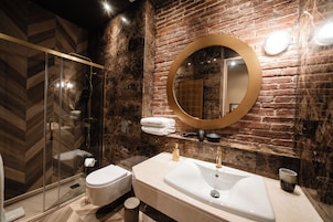 Une salle de bain moderne avec une douche à parois de verre, des toilettes blanches et un grand lavabo doté d’un robinet doré.