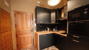 A modern kitchen with wooden cabinets, a black oven, and a herringbone-patterned floor. - Rincón del Conde Suites (León)