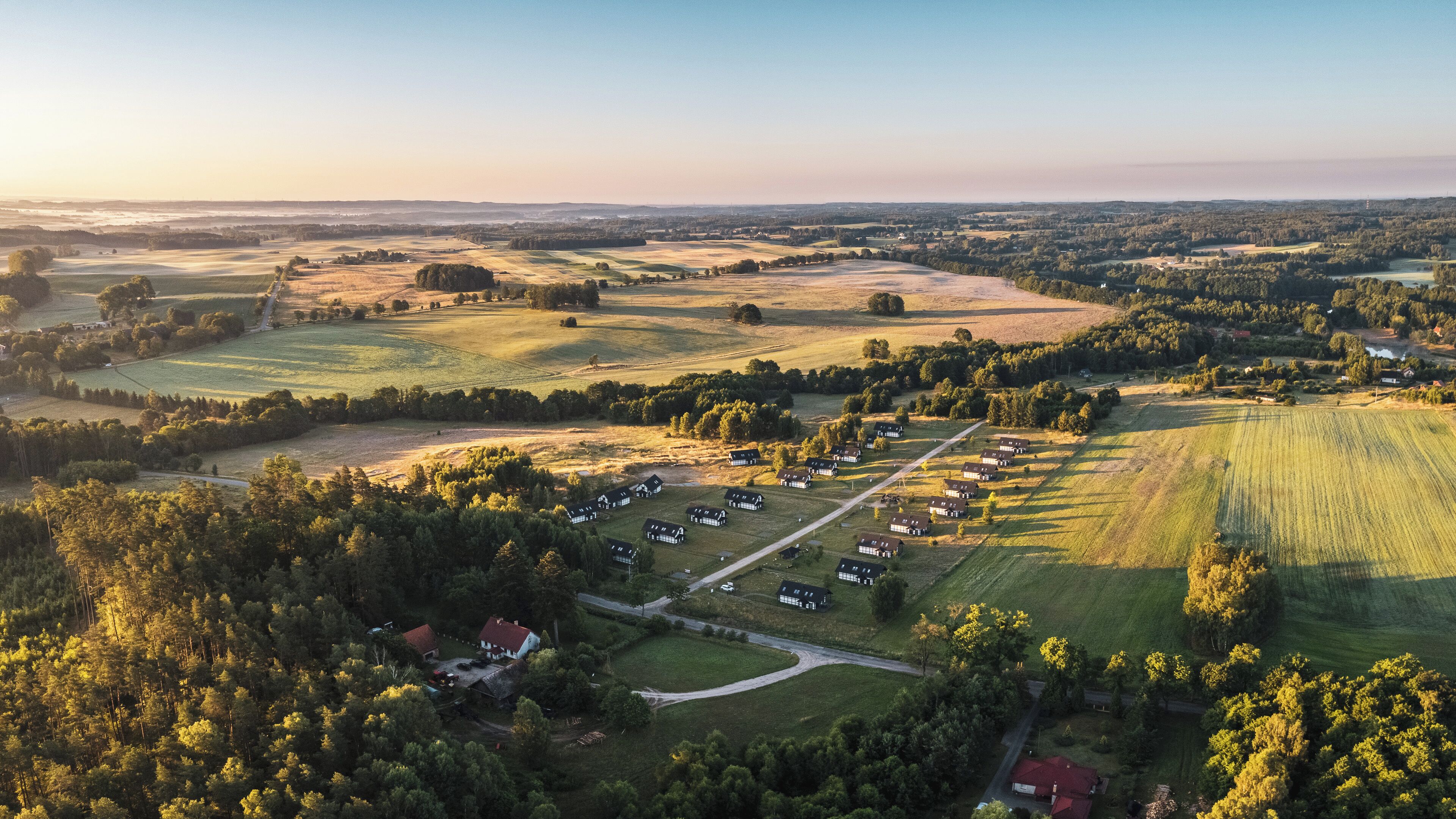 An aerial view of a rural area with a cluster of houses arranged in a grid pattern, surrounded by fields and forests.