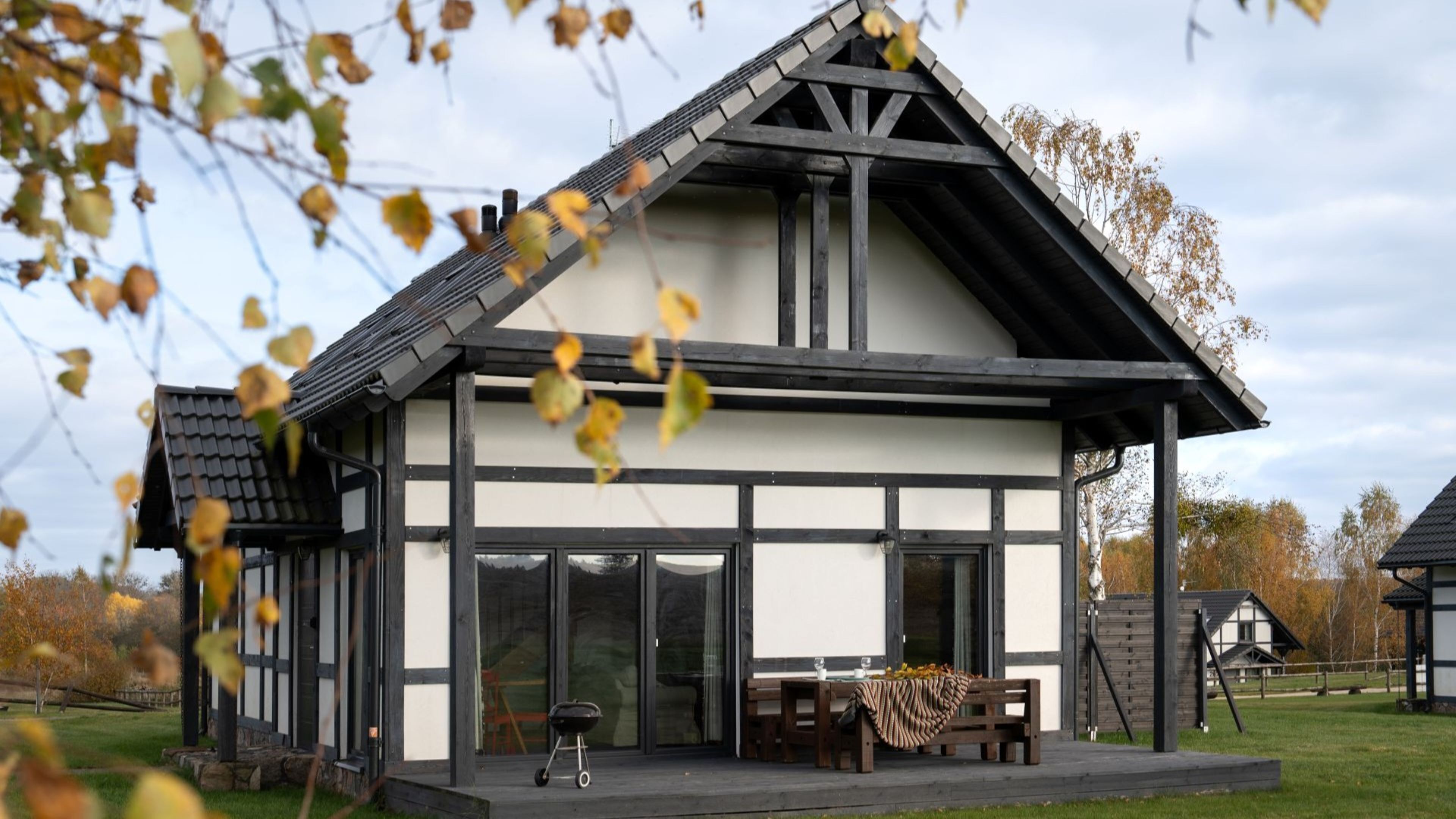 A modern house with a large glass front, a covered patio, and a wooden deck.
