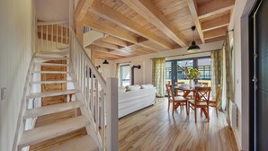 A spacious room with a wooden staircase, a dining area with a table set for four, and a large window with curtains.