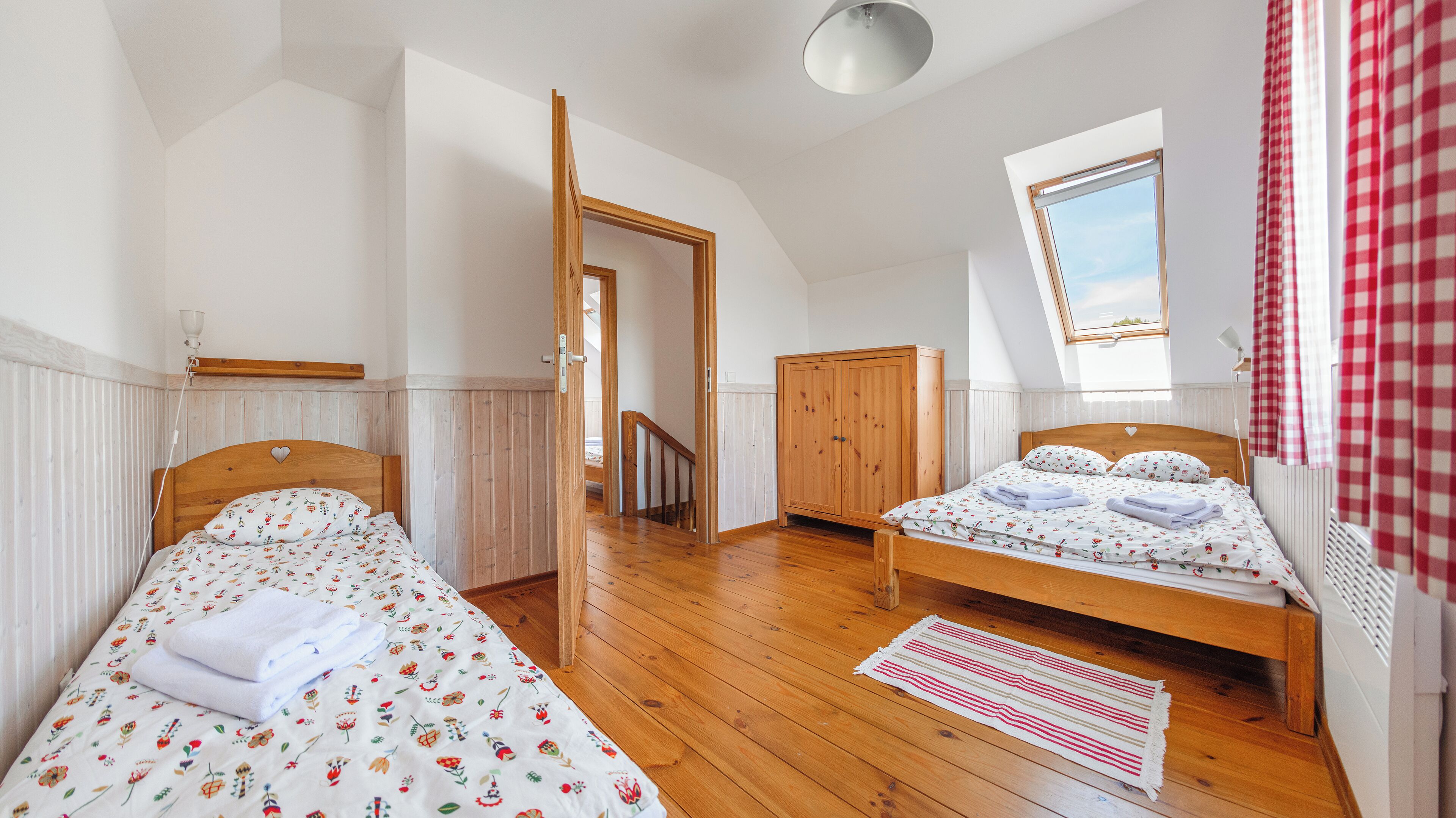 A bedroom with two beds, wooden flooring, a wardrobe, a radiator, and a window with a view.