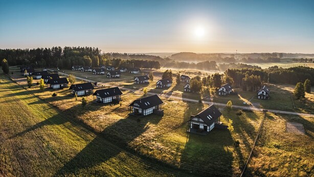 A rural landscape with multiple traditional houses arranged in a pattern, surrounded by fields and trees.