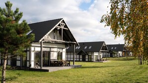 A row of traditional-style houses with pitched roofs and large windows, set in a grassy area with trees.
