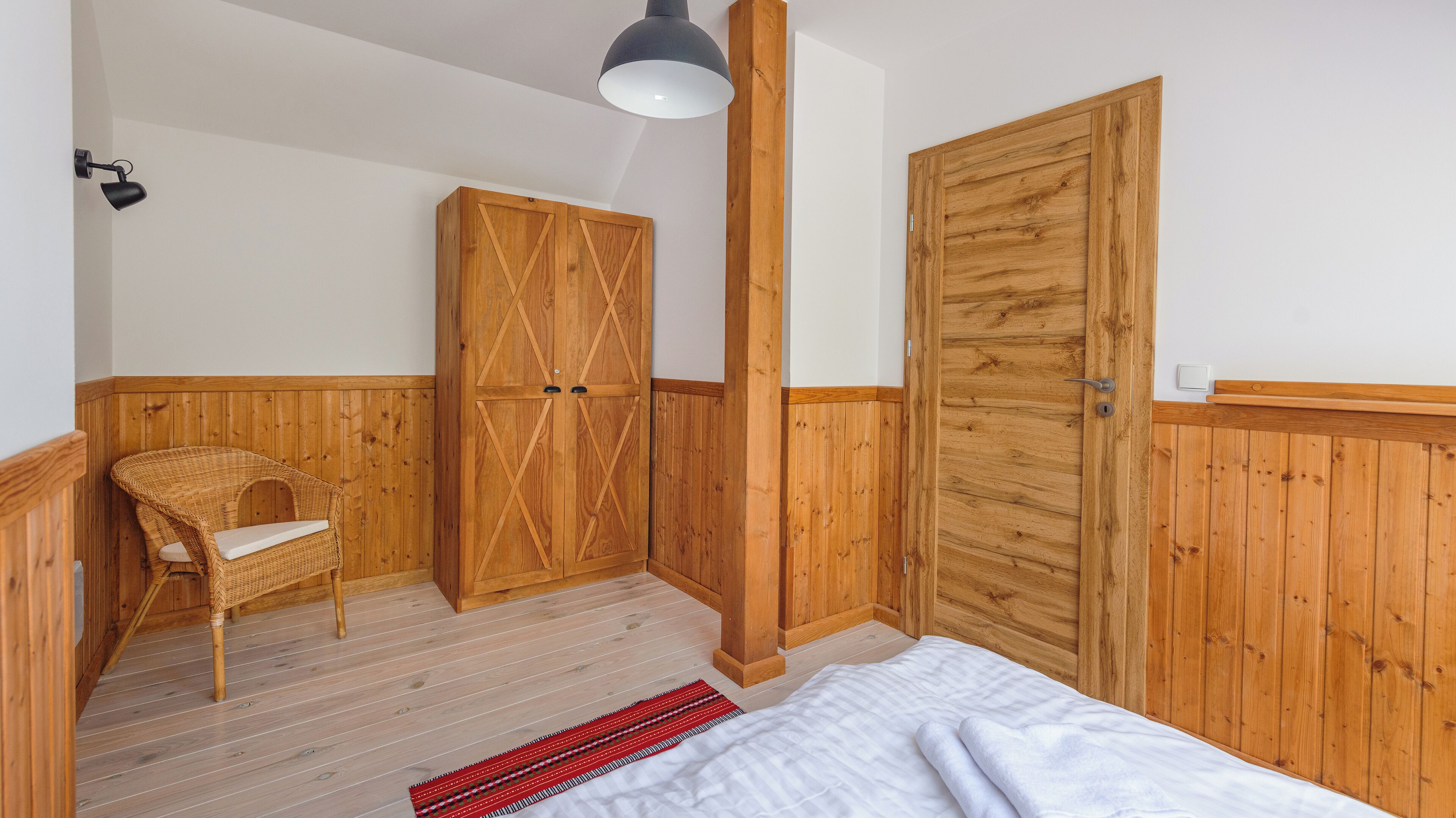 A bedroom with wooden paneling, a bed, a chair, and two wardrobes.