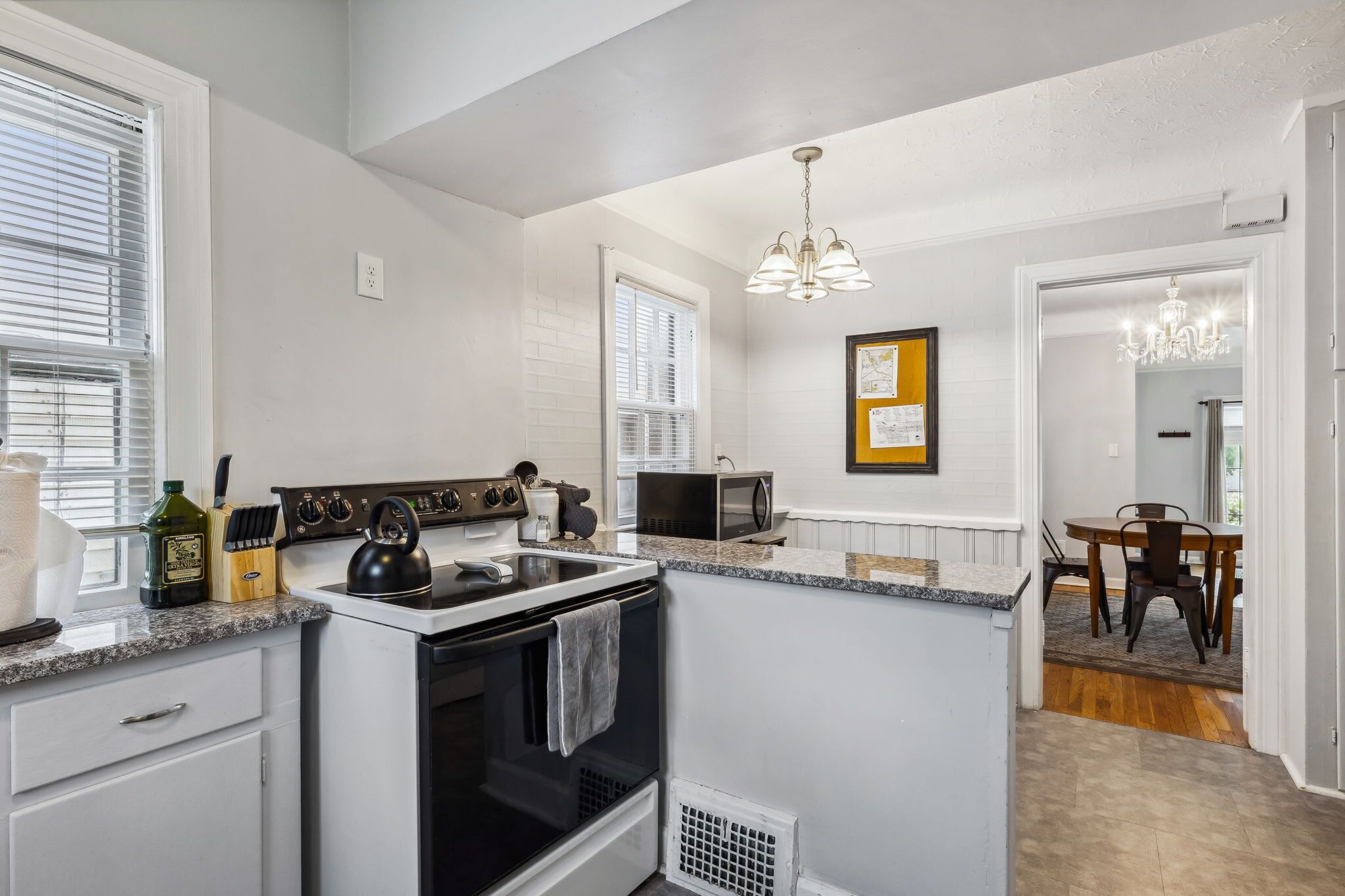 A kitchen with white cabinetry, a black stove, a microwave, and a dining area with a table and chairs.
