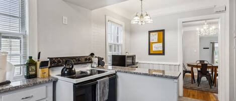 A kitchen with white cabinetry, a black stove, a microwave, and a dining area with a table and chairs.