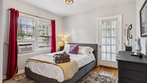 Un dormitorio con cama, mesita de noche, lámpara, cómoda y ventana con cortinas.
