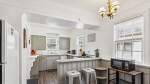 Een keuken met witte kasten, een ingebouwde magnetron en een barkruk.
