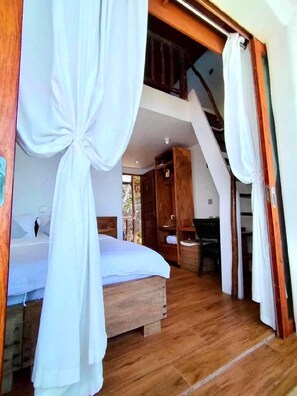 Een slaapkamer met een houten bed, witte gordijnen en een trap die naar een hoger gelegen verdieping leidt.