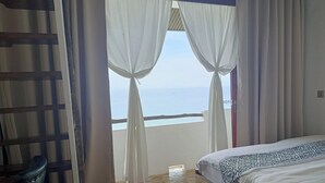 Ein Schlafzimmer mit einem Bett, Holzboden und Meerblick durch durchsichtige Vorhänge.