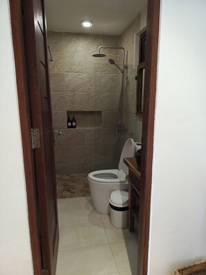 Een kleine badkamer met toilet, douche en een plank met flessen.