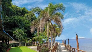 Ein Promenadweg am Strand mit Holzzaun, Palmen und Blick auf das Meer.