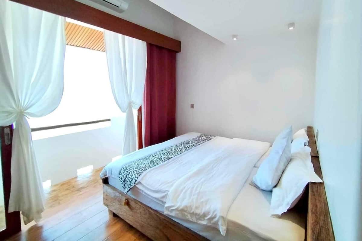 Une chambre à coucher avec un cadre de lit en bois, du linge de lit blanc et une fenêtre ornée de rideaux blancs.