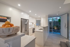 A modern kitchen with a built-in oven, a stainless steel refrigerator, and a large island with a bowl of oranges.