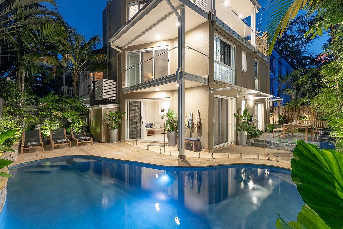 A two-story house with a swimming pool, outdoor seating, and tropical plants.