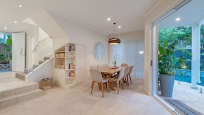 Ein modernes Interieur mit einer Treppe, einem Essbereich mit einem Holztisch und Stühlen sowie einem großen Fenster mit Blick auf Grünflächen.