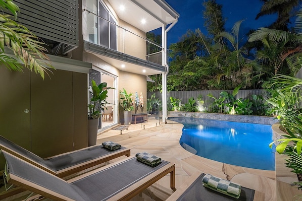 A modern outdoor pool area with lounge chairs and a covered seating area.