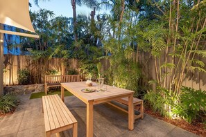 A wooden table set with a pitcher, glasses, and a plate with lime wedges, surrounded by lush tropical plants and a wooden fence. - Little Cove Haven - Naousa 4 with Rooftop deck (Noosa)
