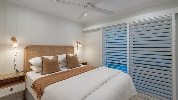 Ein Schlafzimmer mit einem Bett, Nachttischlampen, einem Deckenventilator und einem Fenster mit Jalousien.