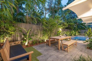 A patio area with a pool, wooden furniture, and lush greenery. - Little Cove Haven - Naousa 4 with Rooftop deck (Noosa)
