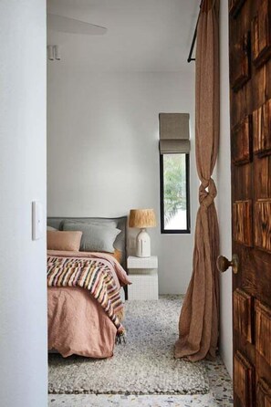 Ein Schlafzimmer mit einem Bett, einem Nachttisch, einer Lampe und einem Fenster.