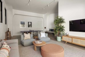 A modern living room with a sofa, ottoman, coffee table, and a dining area with a table and chairs.