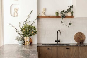 A kitchen with a marble countertop, wooden cabinets, a black faucet, and various potted plants.
