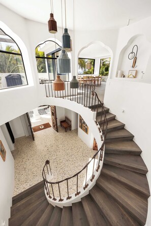 A spacious interior with a curved staircase, multiple hanging pendant lights, and a view of the outdoors through large windows. - Mykonos Luxury Villa at Sunshine Beach (Noosa)