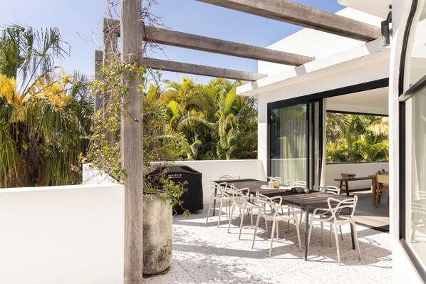 An outdoor patio with a table and chairs, surrounded by lush greenery and a modern building.
