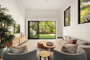 A modern living room with a sofa, a coffee table, and a TV. There is a sliding glass door leading to a garden.