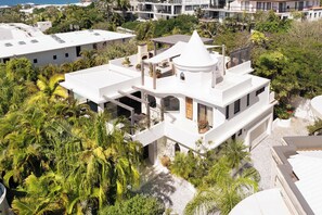A modern multi-story house with a white exterior, surrounded by lush greenery and palm trees. - Mykonos Luxury Villa at Sunshine Beach (Noosa)